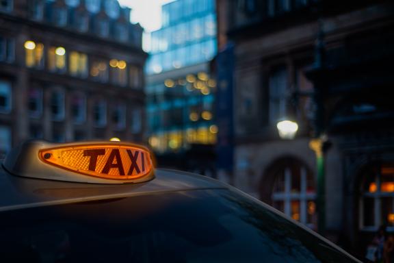 A close-up of an illuminated orange taxi sign mounted on the roof of a vehicle.