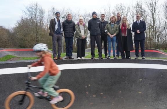 Child on BMX bike riding past a group of Council representatives at BMX track