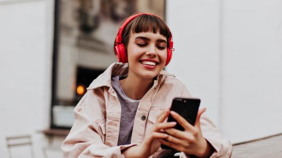 Photo of young woman using her mobile phone while wearing red headphones on