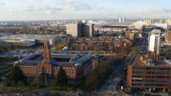 Aerial view of Trafford Town Hall with clock tower, surrounding streets, and Old Trafford stadium in the background.