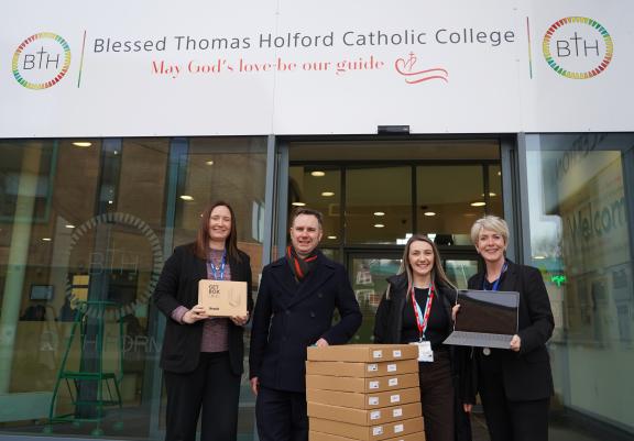 Four people, including Jane Slater and Tom Ross with laptops outside Blessed Thomas Holford RC School