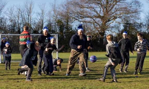A group of children and adults play an energetic outdoor game on a grassy field