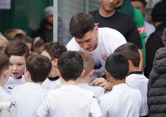 A group of young football players gather around an adult coach in a white shirt during a training session