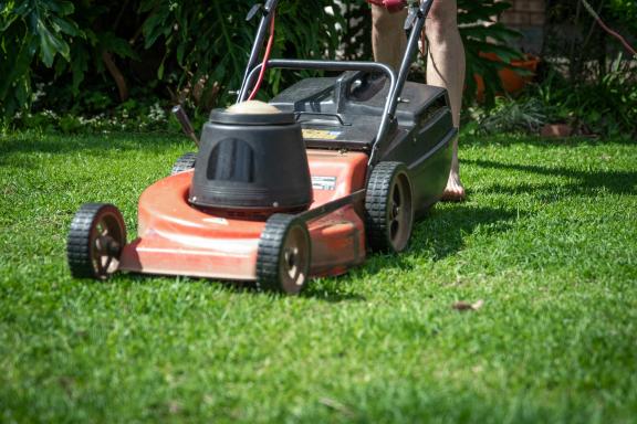 An orange lawnmower being pushed along a lawn
