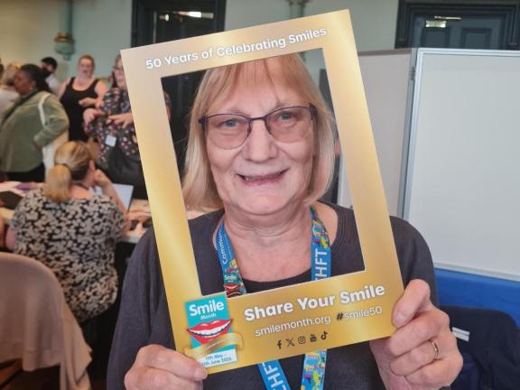 Jacqui Delaney holds a gold photo frame labelled “50 Years of Celebrating Smiles” and “Share Your Smile” with “Smile Month” branding