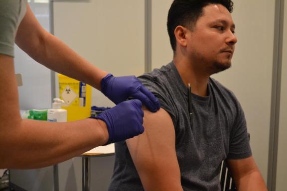A man with his sleeve rolled up as a nurse wearing surgical gloves prepares to inject a vaccination