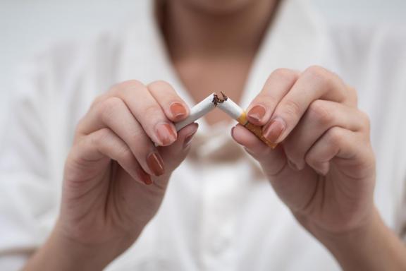 Close-up of a person’s hands breaking a cigarette in half, with tobacco visible at the snapped centre.