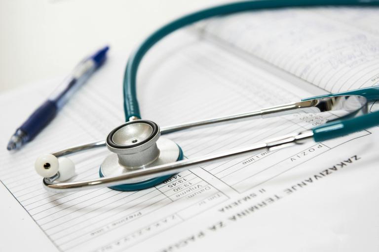 A teal stethoscope resting on an open medical chart with a pen nearby.