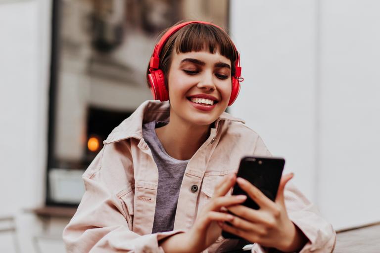 Photo of young woman using her mobile phone while wearing red headphones on
