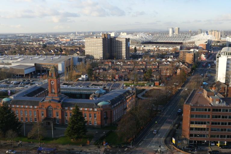 Aerial view of Trafford Town Hall with clock tower, surrounding streets, and Old Trafford stadium in the background.