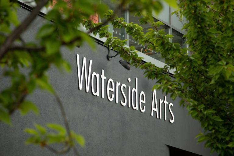 A sign on the outside of a building. The words say 'Waterside Arts'