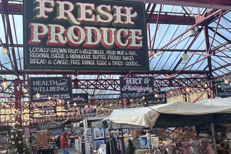 Indoor market with red metal beams and a glass roof, featuring a large “Fresh Produce” sign advertising locally grown goods