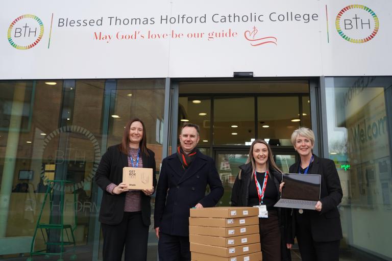 Four people, including Jane Slater and Tom Ross with laptops outside Blessed Thomas Holford RC School