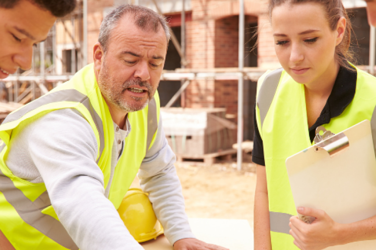 Four people in high-vis in a construction setting all looking at a diagram