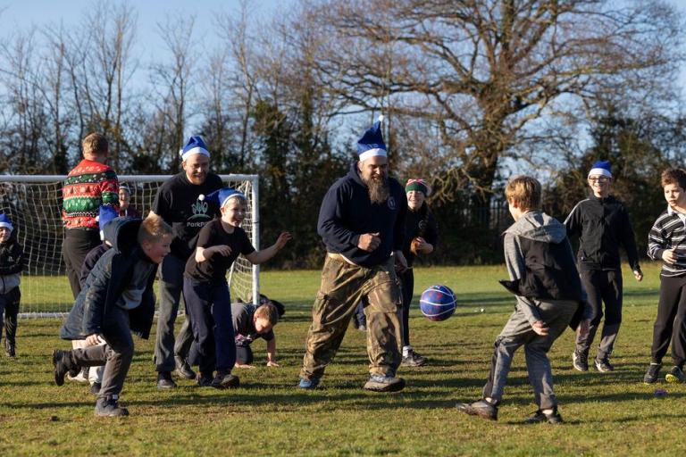 A group of children and adults play an energetic outdoor game on a grassy field