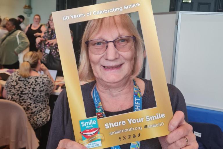 Jacqui Delaney holds a gold photo frame labelled “50 Years of Celebrating Smiles” and “Share Your Smile” with “Smile Month” branding