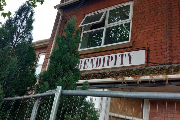 A dilapidated building wthat has been boarded up, surrounded by metal fencing