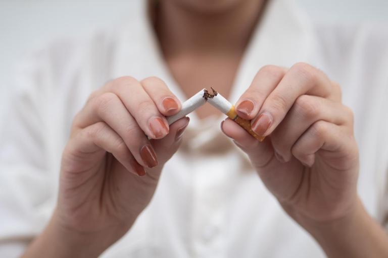 Close-up of a person’s hands breaking a cigarette in half, with tobacco visible at the snapped centre.